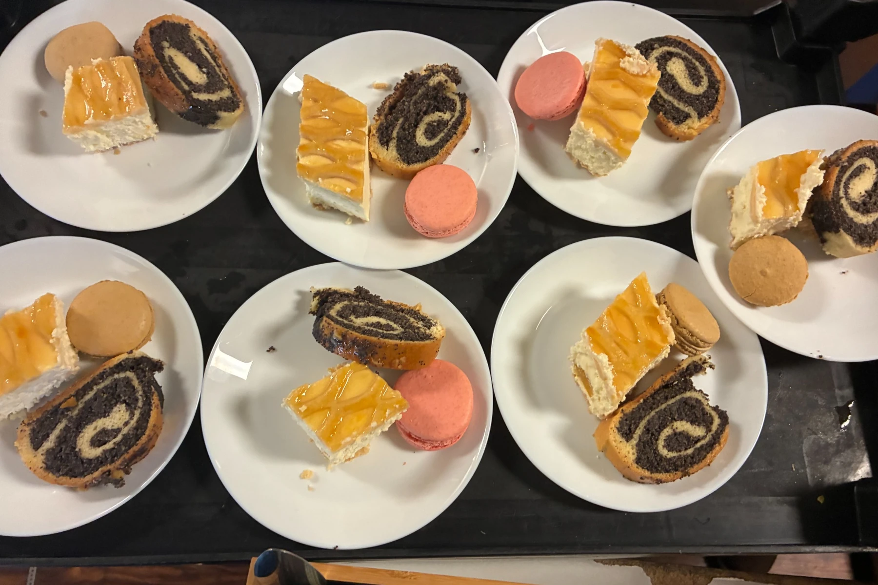 Overhead view of plated event desserts on a serving cart, with each plate featuring cheesecake, poppy seed roll, and a colorful macaron.