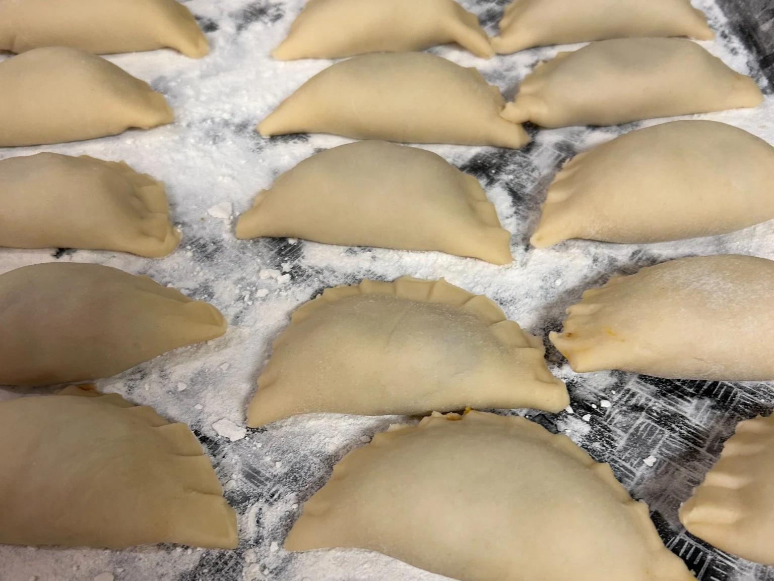 Fresh handmade pierogies lined up on a floured tray before cooking for a Kat's Café & Restaurant catering order.