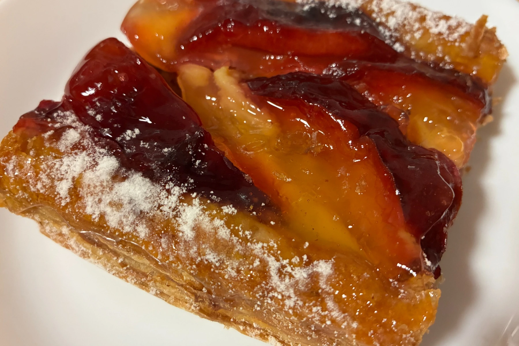 Fresh plum pastry with glossy baked plums over flaky pastry and a light dusting of powdered sugar.