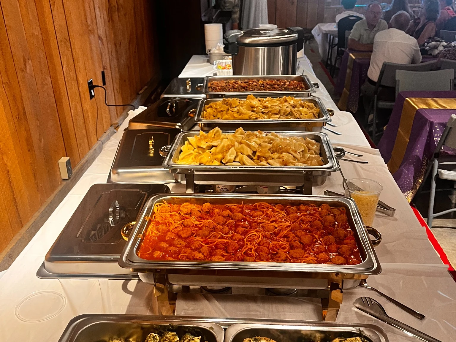 Long buffet catering setup with chicken, spaghetti and meatballs, pierogies, and chafing dishes at a private event.
