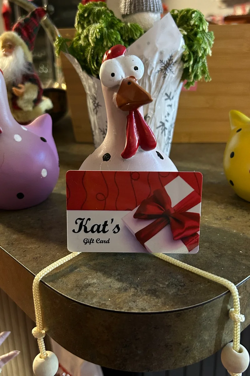 Decorative rooster with a Kat’s Café & Restaurant gift card displayed on a café shelf.