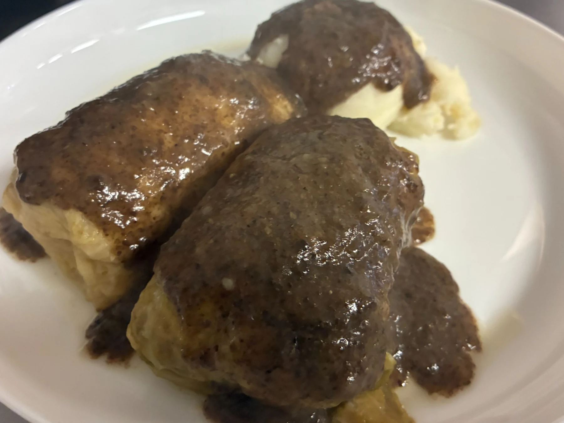 Two XL halupki with homemade mushroom sauce served over mashed potatoes served on a white plate.