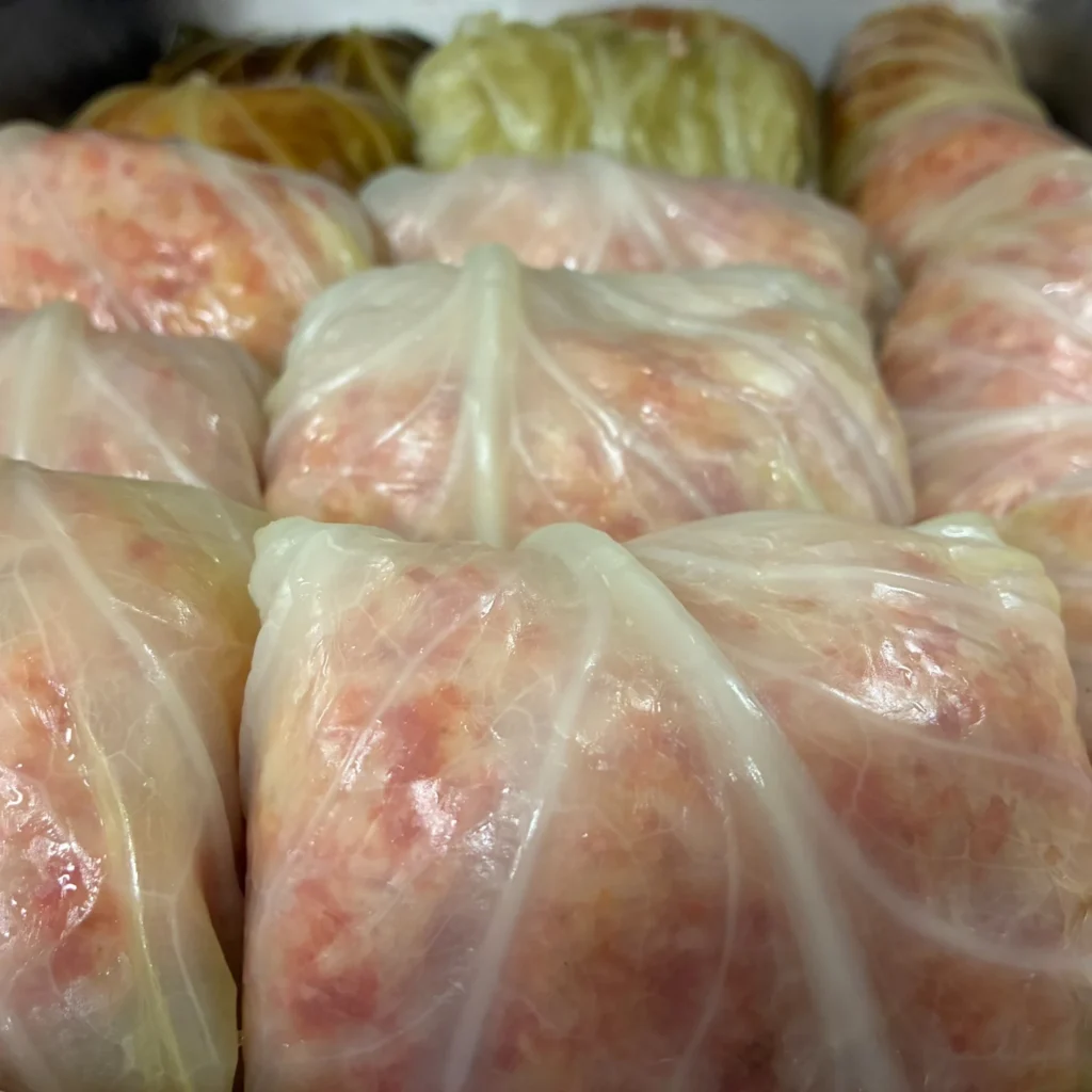Rows of uncooked halupki wrapped in tender cabbage leaves in a deep catering pan.