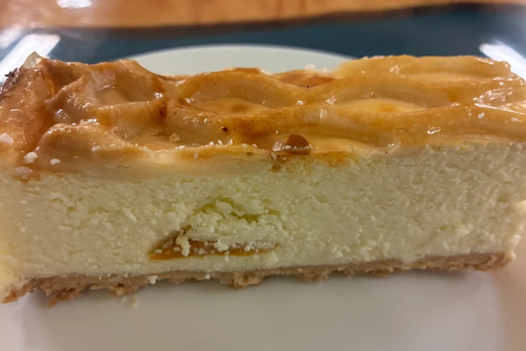 Slice of homemade baked peach cheesecake with a creamy filling, fruit swirls, and a golden top.