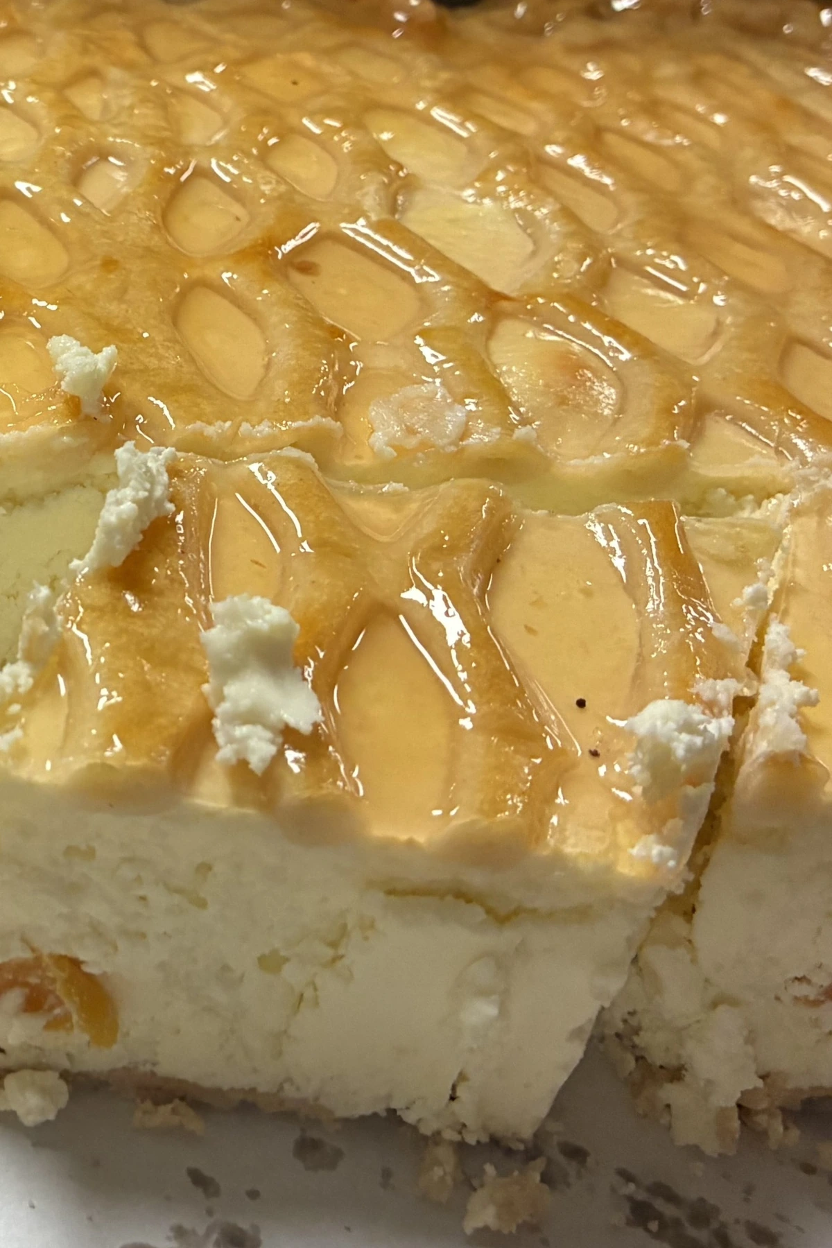 Homemade baked cheesecake with pineapple and peach pieces, topped with a glossy glazed pattern and shown in thick sliced squares.