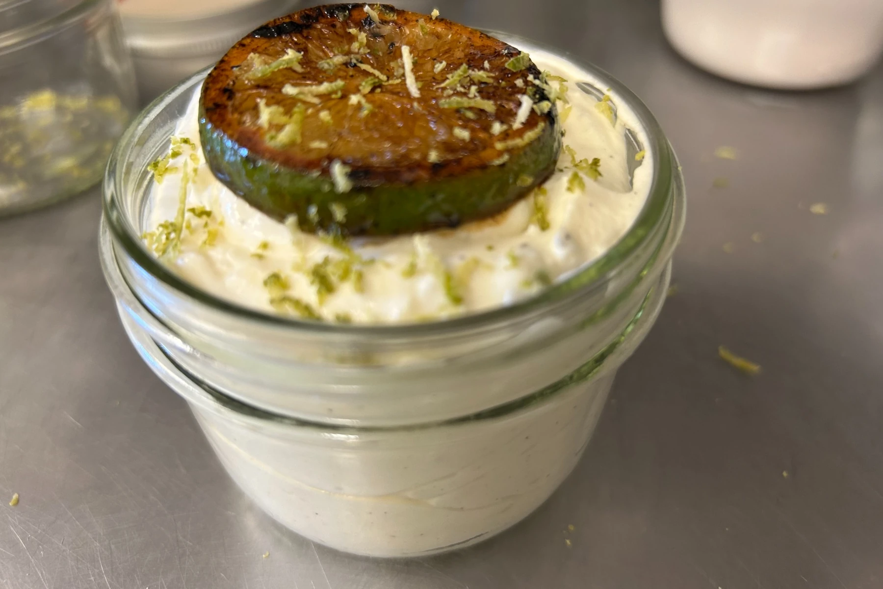 Key lime cheesecake dessert in a mason jar topped with whipped cream, a brûléed lime slice, and fresh lime zest.