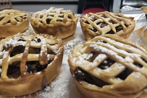Mini lattice-top fruit pies dusted with powdered sugar and arranged on a tray.