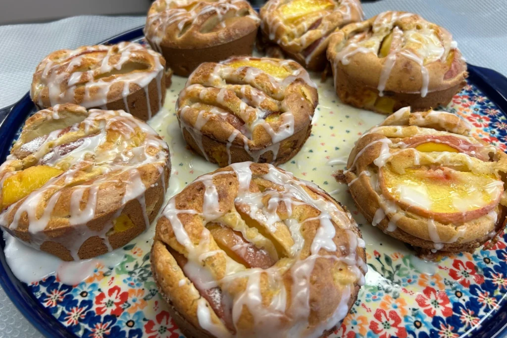 Peach mini cake muffins baked with fruit slices and drizzled with sweet icing on a decorative platter.