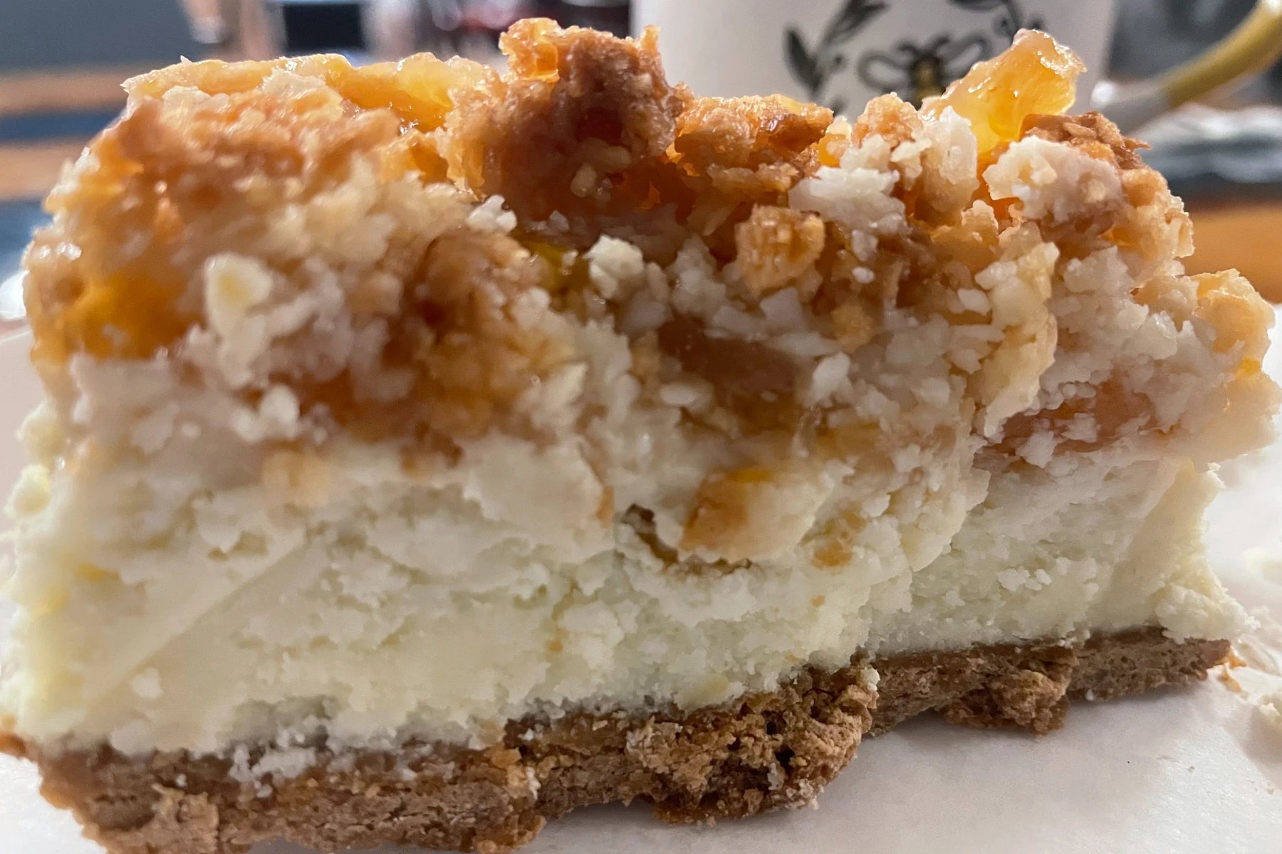 Slice of pineapple coconut cheesecake with creamy filling and toasted coconut crumble on a crumb crust.