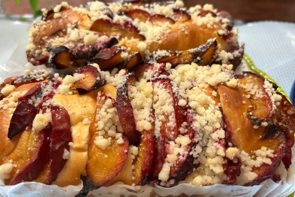 Homemade plum cake topped with sliced plums and buttery crumb streusel, shown fresh from the bakery case.