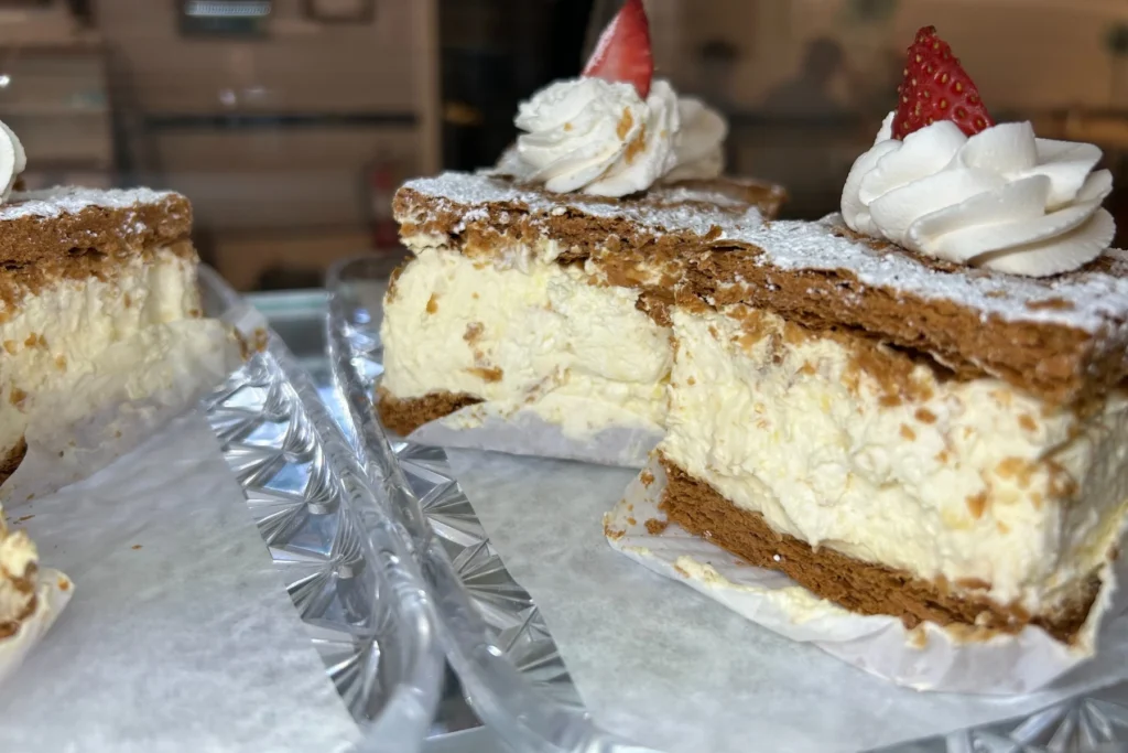 Cream-filled puff pastries layered with flaky pastry, powdered sugar, and whipped cream.