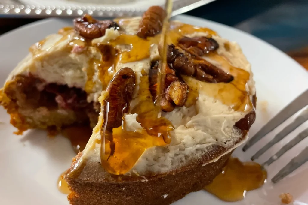 Pumpkin cranberry mini cake with cream cheese frosting, toasted pecans, and a drizzle of Pennsylvania maple syrup on a white plate.