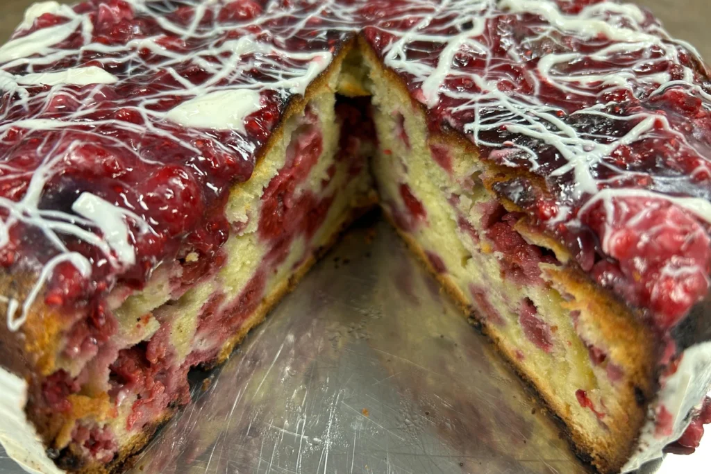 Raspberry cake with a glossy berry topping and white icing drizzle, cut open to show the fruit-filled interior.