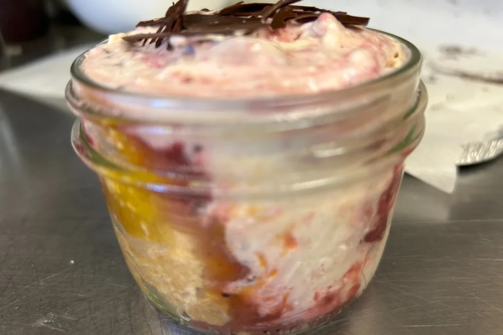 Mason jar dessert layered with seasonal pumpkin cheesecake, berries, cake, and chocolate shavings.