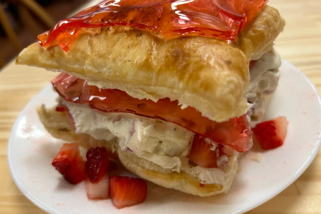 Filled pastry dessert with real cream, strawberry pieces, and cherry gelatine served on a white plate.