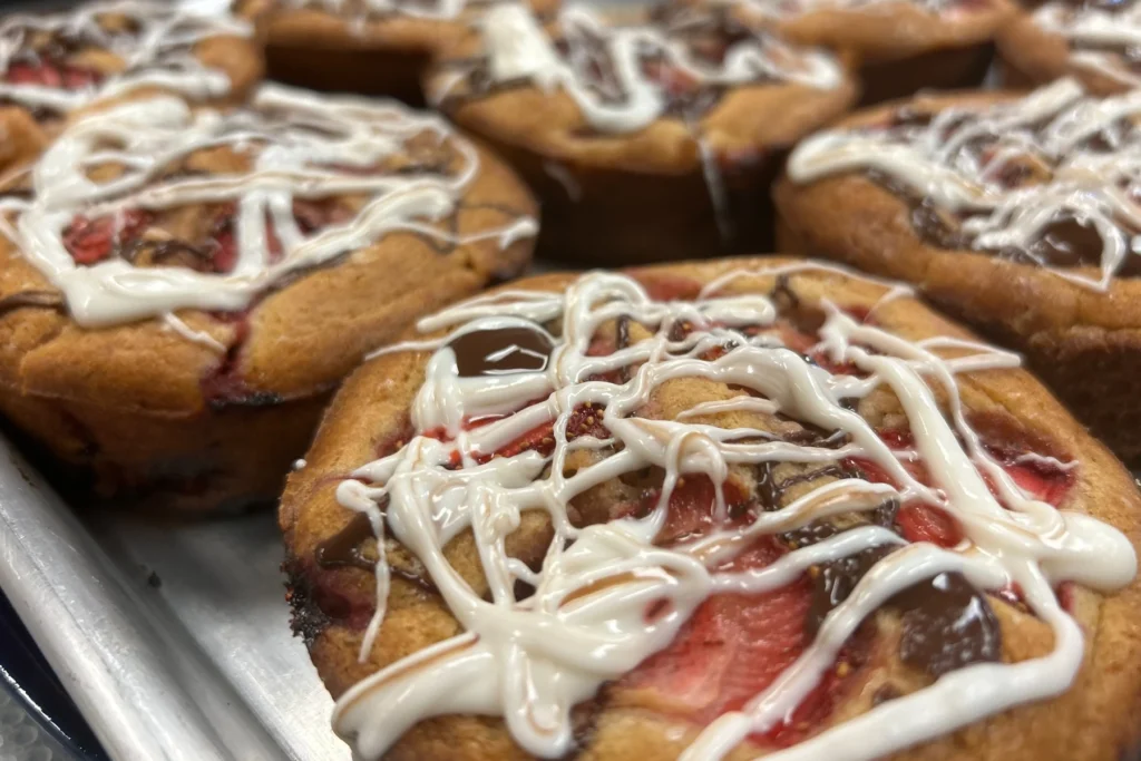 Fresh strawberry mini cakes drizzled with white icing and chocolate, arranged on a tray.