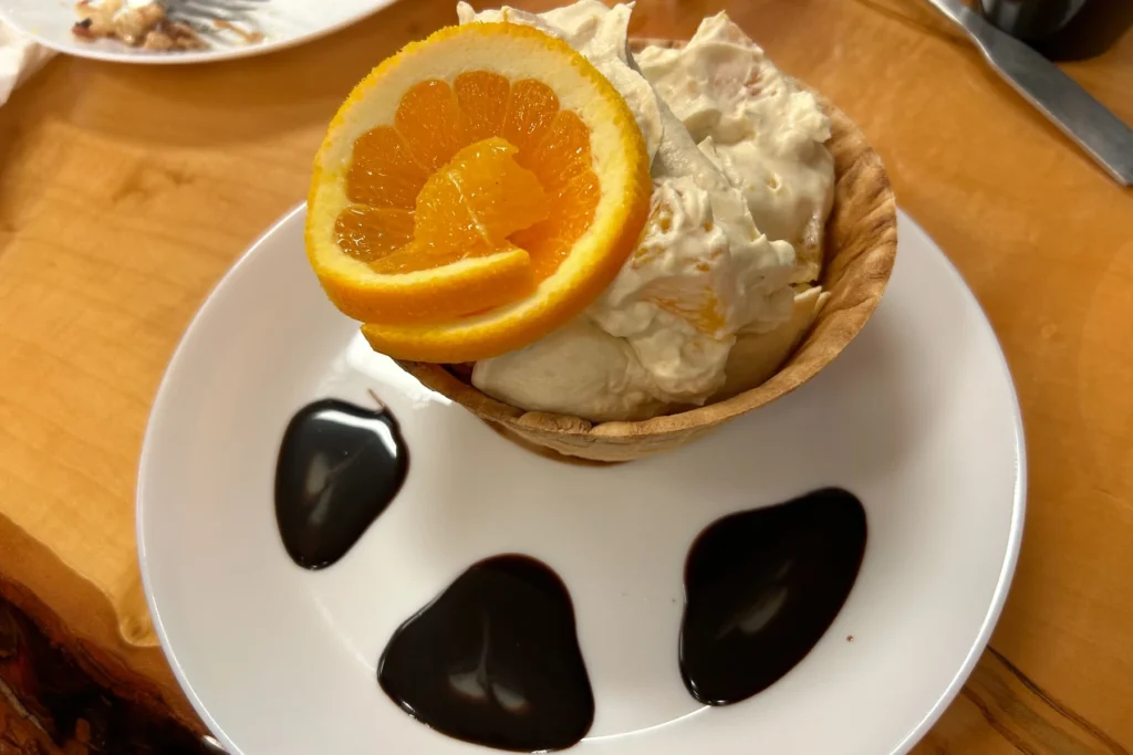 Sweet cream dessert served in a homemade waffle bowl with orange slices and chocolate sauce.