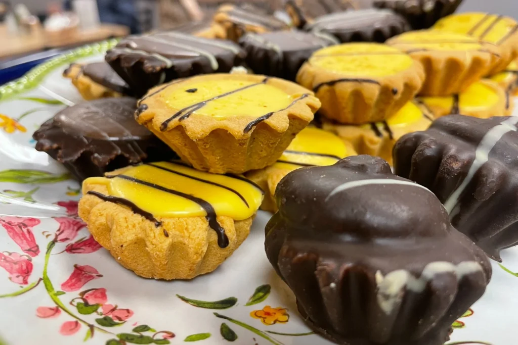 Assorted tea cookies with lemon glaze and chocolate coatings displayed on a floral platter.