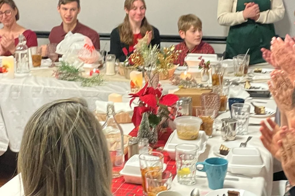 Guests seated around a holiday table during Kat’s Café & Restaurant’s Polish Holy Supper, with festive decorations and applause.