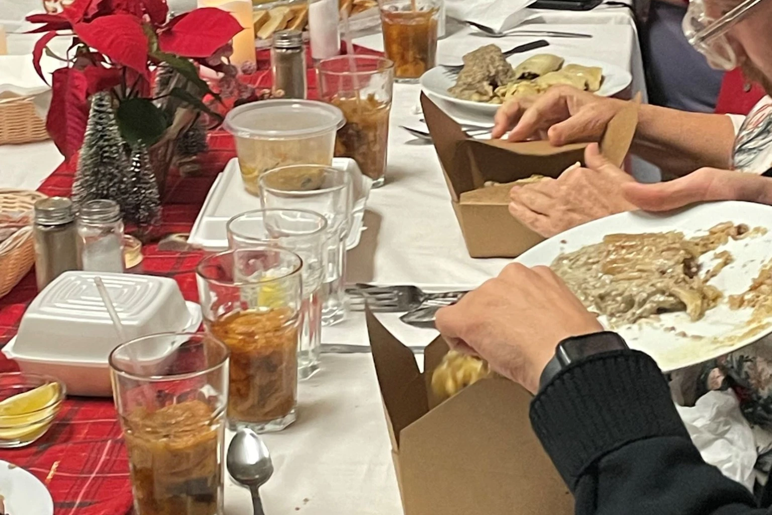 Close view of the holiday table at Kat’s Café & Restaurant’s Polish Holy Supper, showing plates, drinks, decorations, and take-home food boxes.