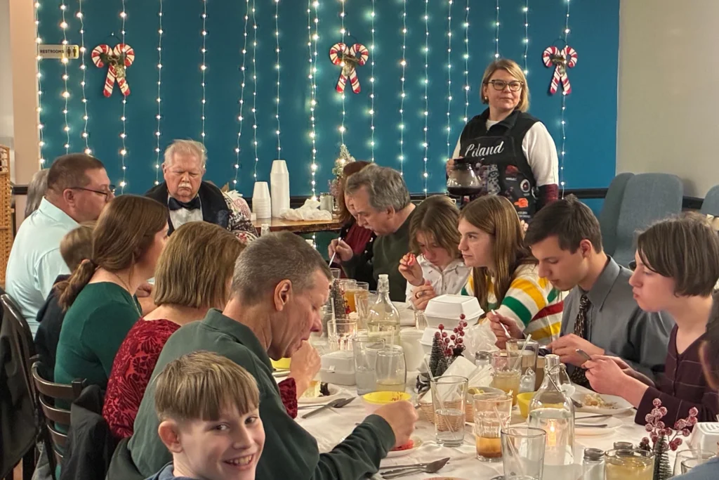 Guests gathered at a long holiday table while a host stands near a wall of string lights at Kat’s Café & Restaurant.