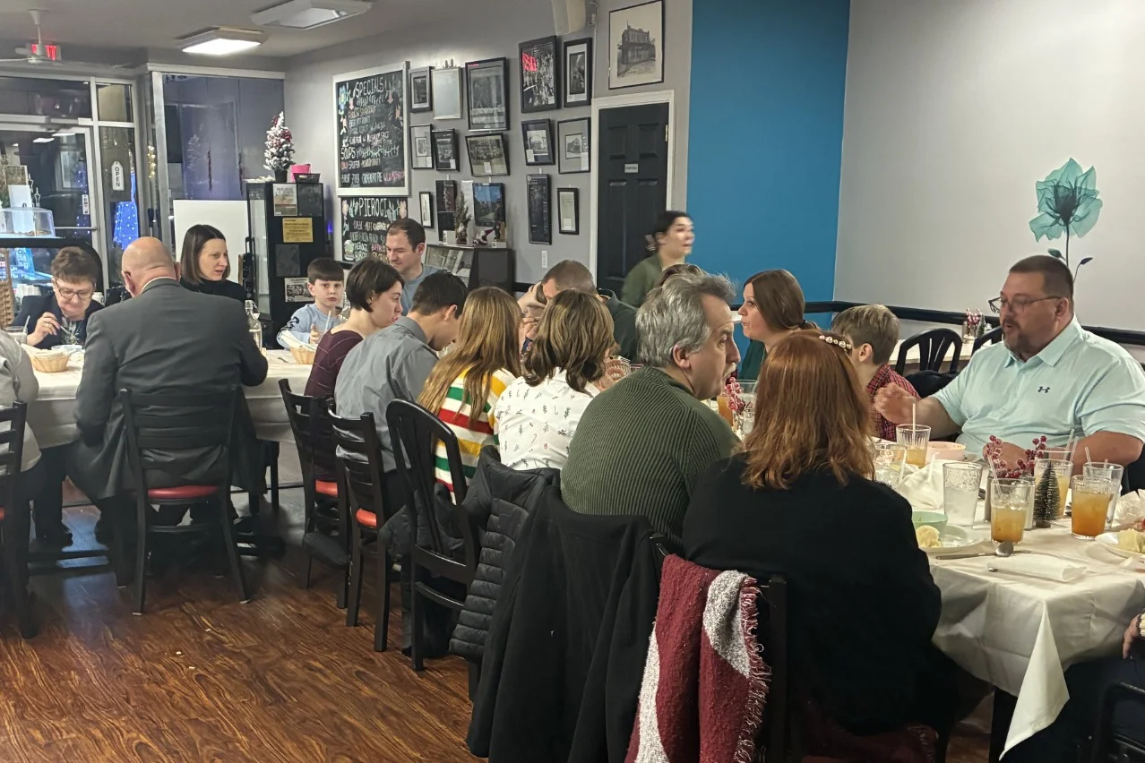Wide room view of guests sharing Kat’s Café & Restaurant Christmas Eve Holy Supper around connected tables.