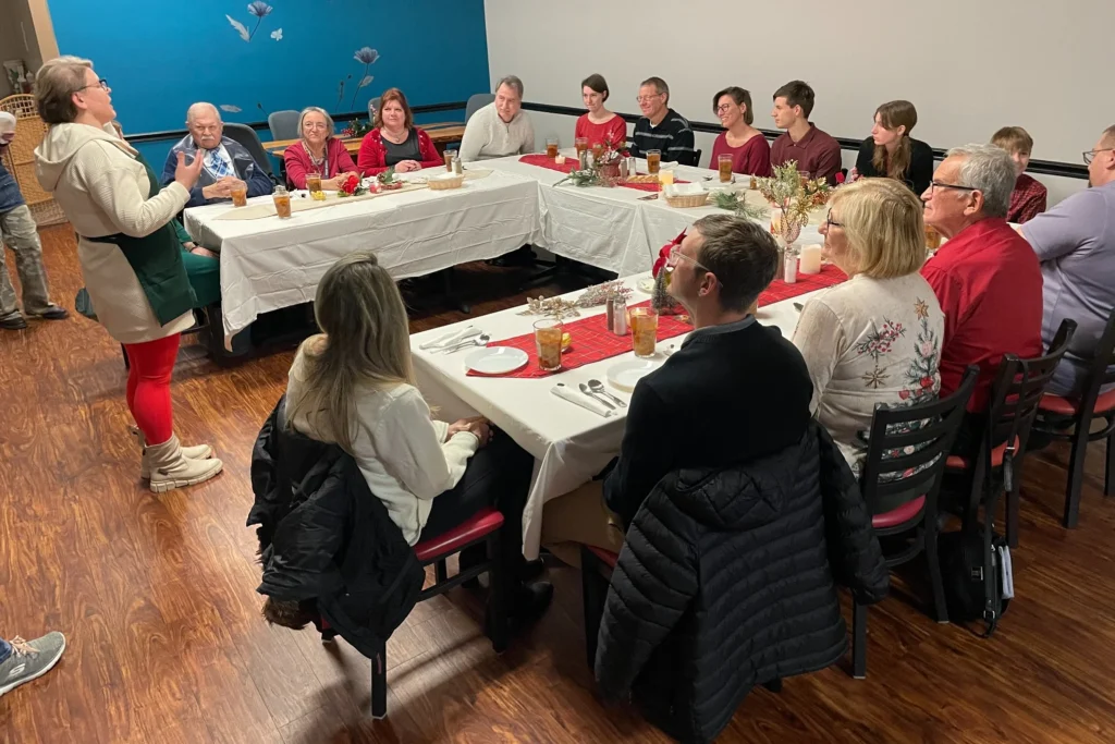 Guests seated around U-shaped tables while Chef Kat addresses the room during a holiday supper at Kat’s Café & Restaurant.