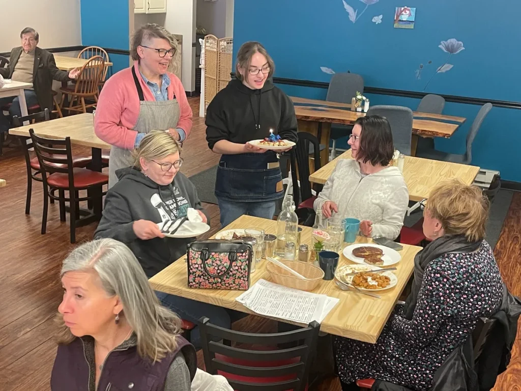 Staff member serving dessert to guests seated around a table at Kat’s Café & Restaurant.