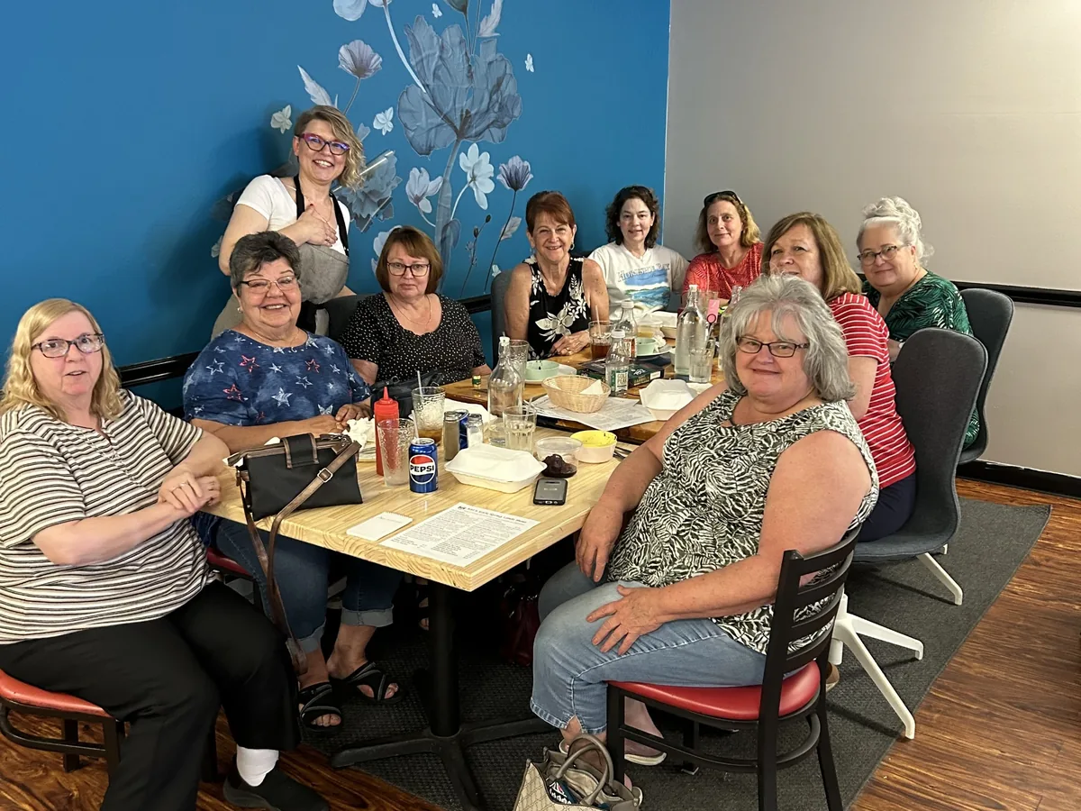 Large group of guests gathered for a meal at the custom-made dining table by the blue floral mural at Kat’s Café & Restaurant.