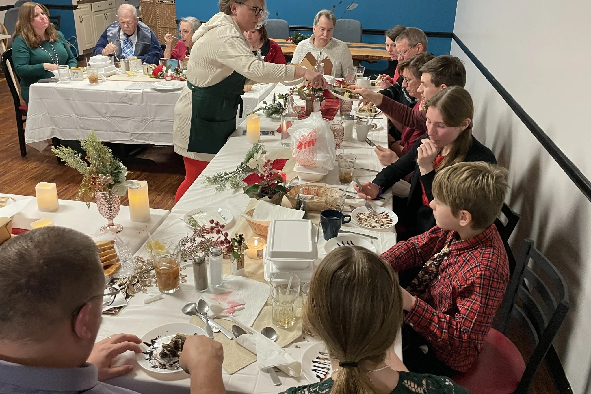 Chef Kat serving dessert strudel to guests seated at a festive table during a Christmas Eve Holy Supper at Kat’s Café & Restaurant.