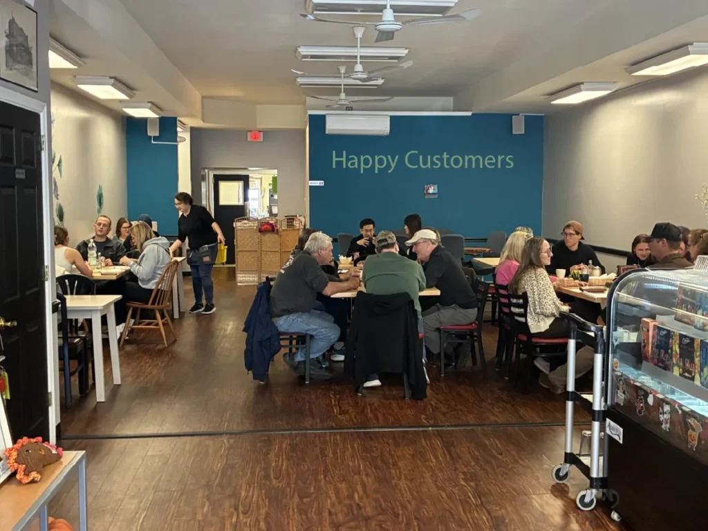 Dining room at Kat’s Café & Restaurant with guests of different ages and races happily seated at tables enjoying meals together.