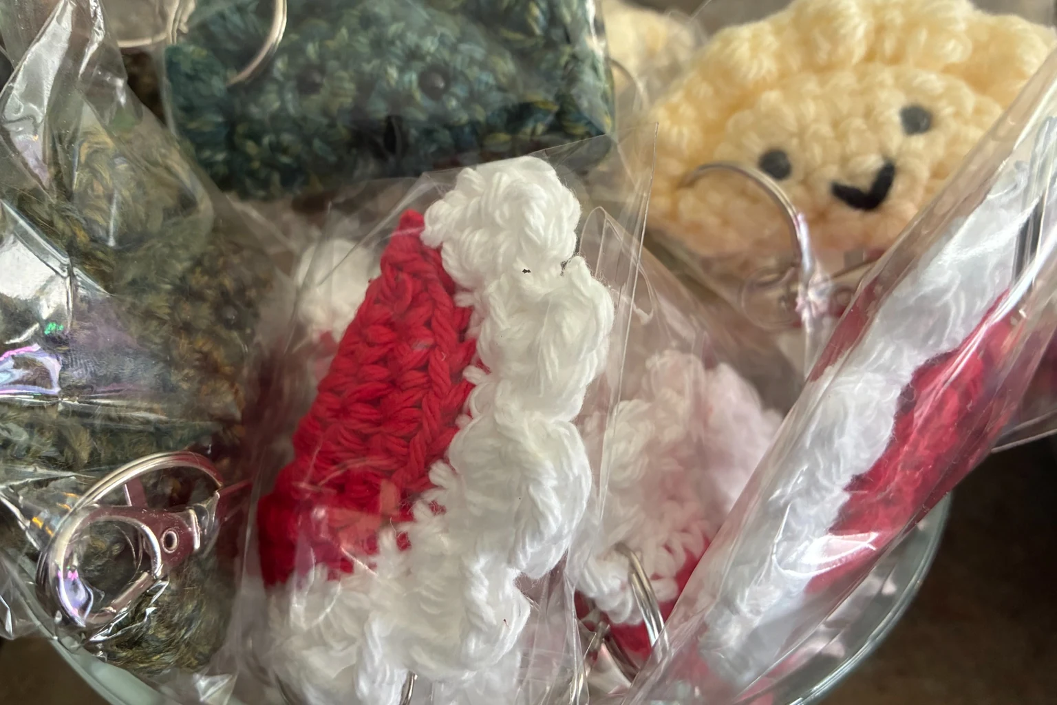 Packaged crochet keychains bowl close-up at Kat’s Close-up of assorted packaged crochet keychains and a red-and-white crochet keychain in a glass bowl at Kat’s Café & Restaurant.