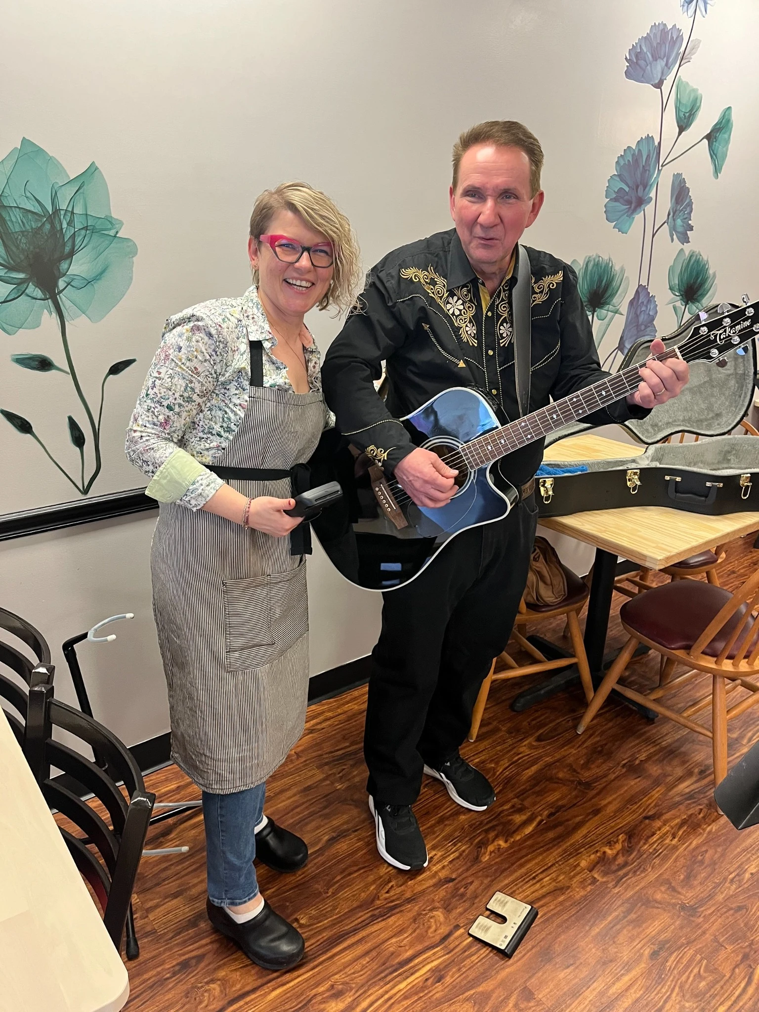 A smiling Chef Kat in an apron poses with a guitarist during a live music event at Kat’s Café & Restaurant.