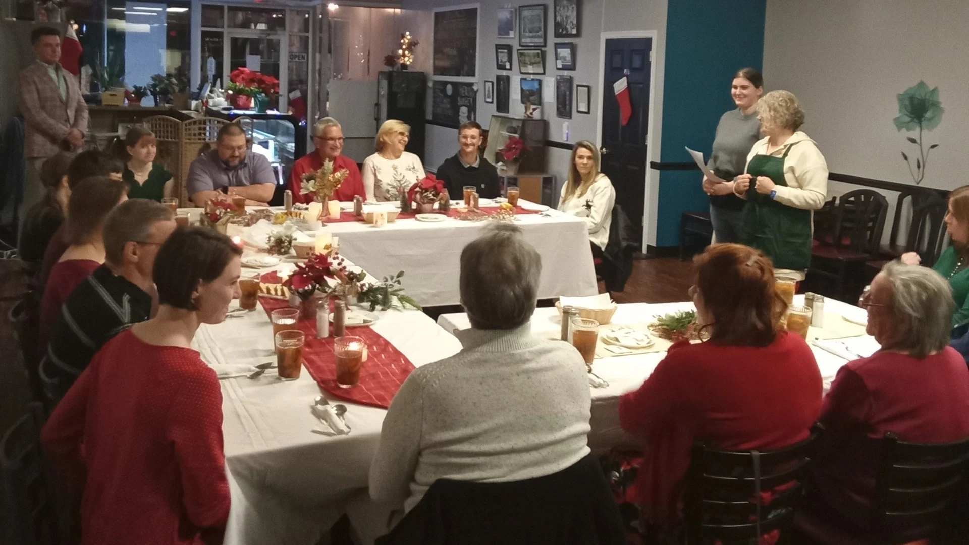 Guests from near and far share a Christmas Eve supper at a long table inside Kat’s Café with holiday lights and decorations.