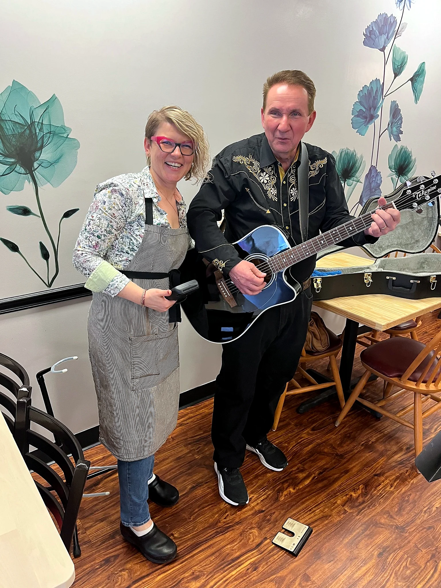 A smiling Chef Kat in an apron poses with a guitarist during a live music event at Kat’s Café & Restaurant.