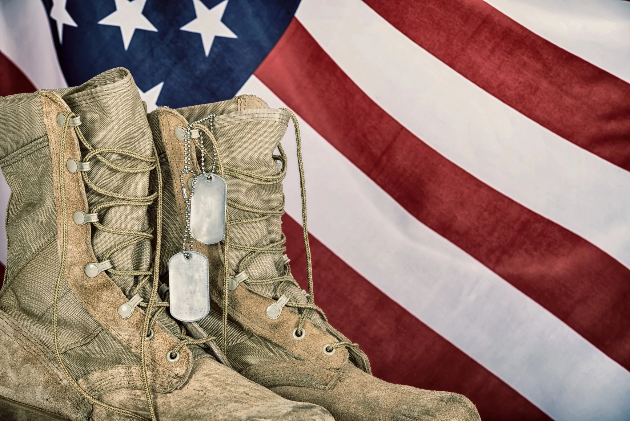 Tan military combat boots with dog tags displayed in front of an American flag for Veterans Day.