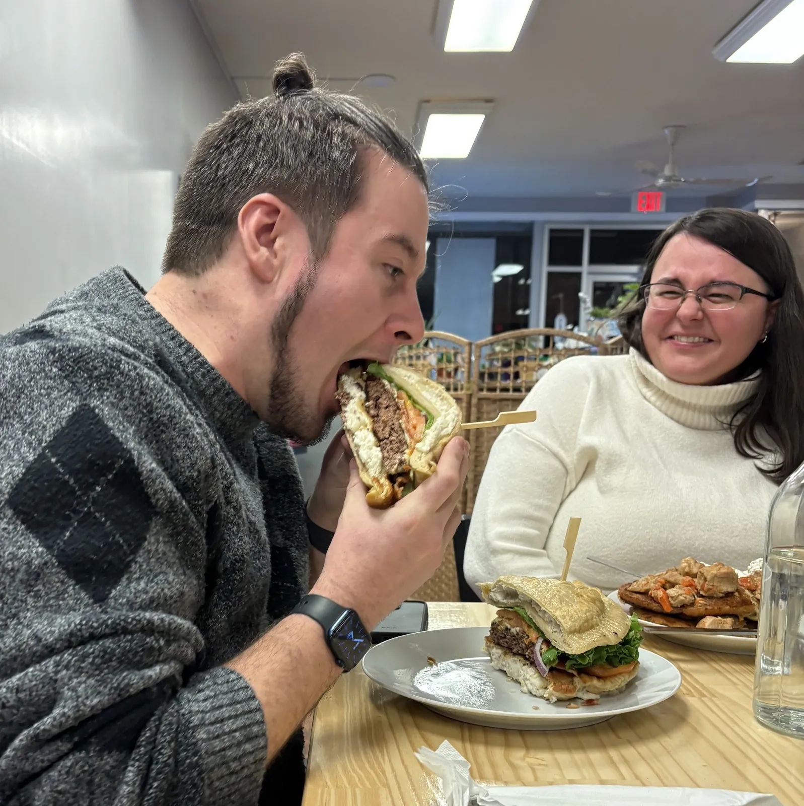 Guest taking a bite of Kat’s Café & Restaurant Pierogi Burger while another guest smiles at the table.