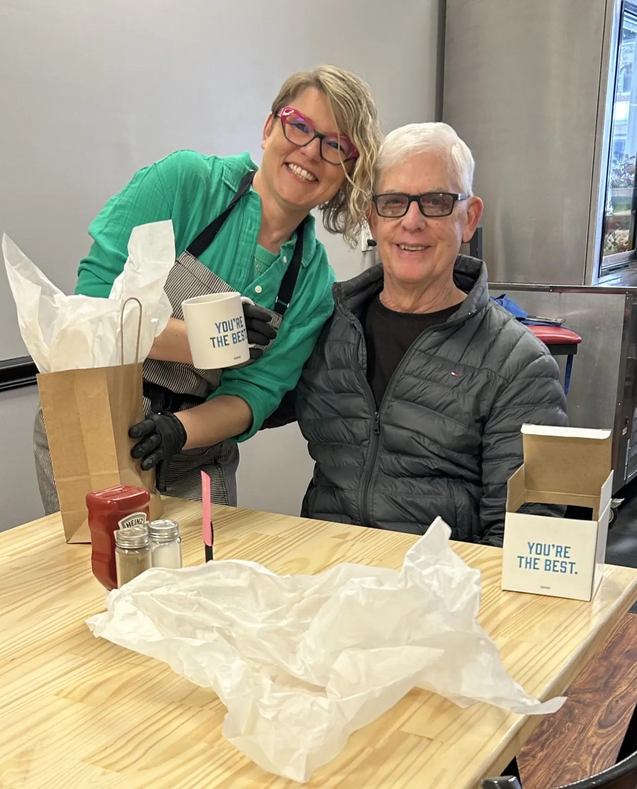 Chef Kat posing with a guest inside the restaurant after having received a thank you gift mug with the words "you're the best."