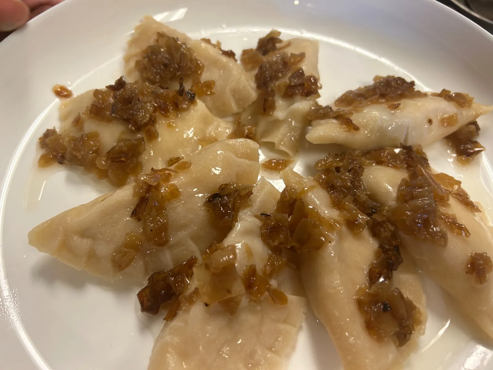 Close-up of handmade boiled pierogies at Kat’s Café & Restaurant, topped with golden-brown caramelized onions on a white plate.