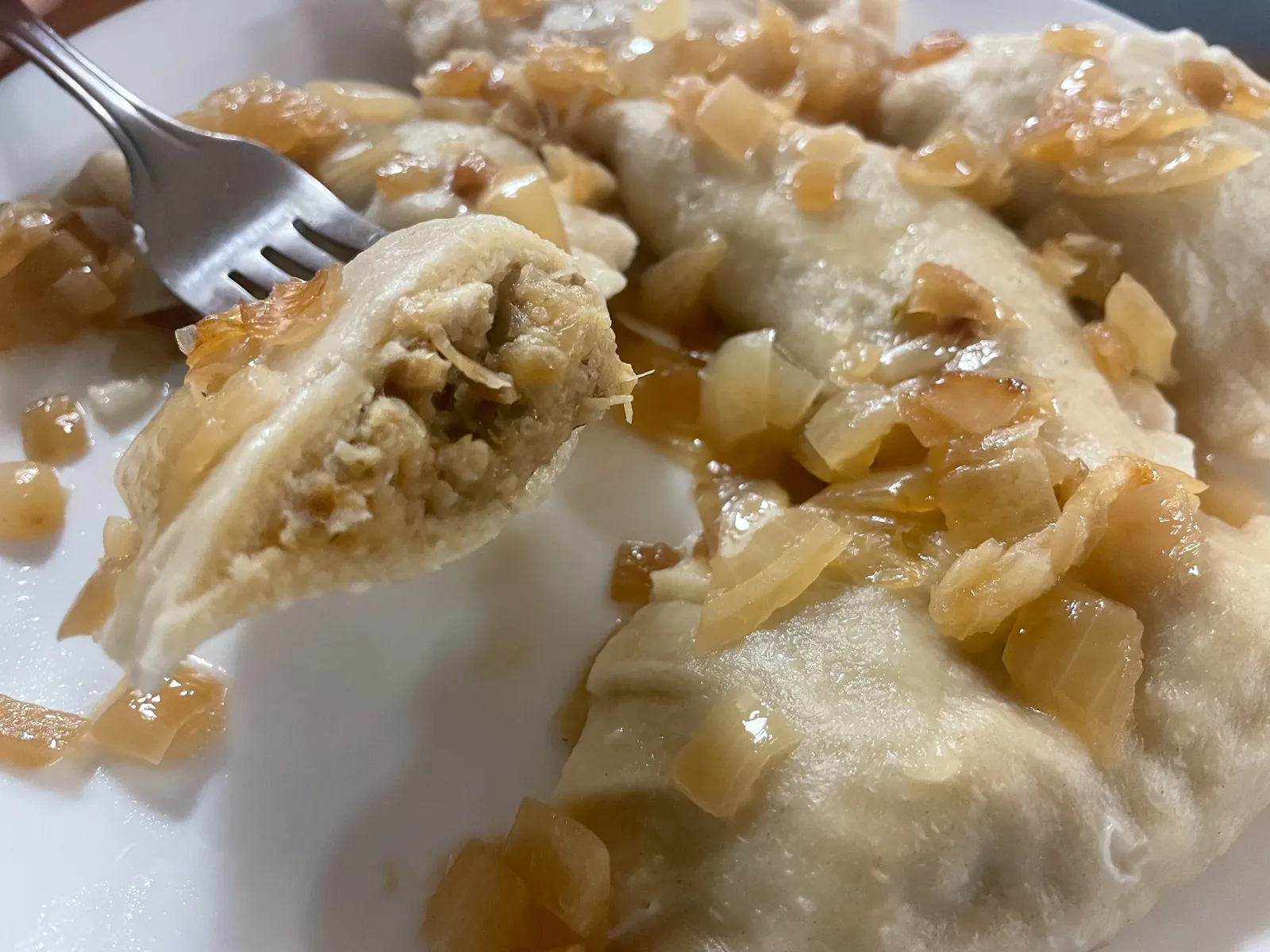 Close-up of a cabbage and mushroom pierogi on a fork above boiled pierogies topped with sautéed onions at Kat’s Café & Restaurant.