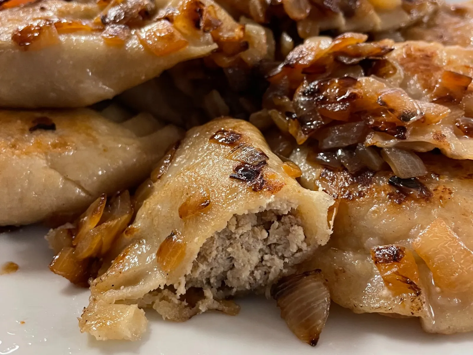Close-up of a cut-open meat pierogi surrounded by pan-fried pierogies topped with sautéed onions at Kat’s Café & Restaurant.