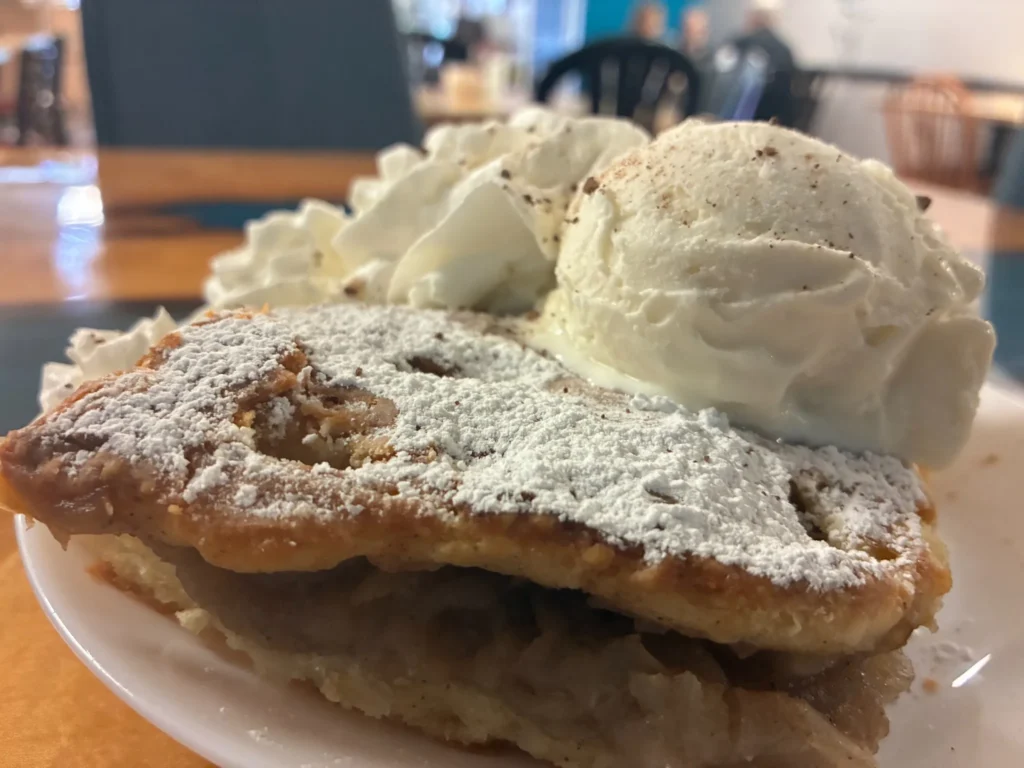 Slice of apple pie topped with powdered sugar and served with vanilla ice cream and whipped cream at Kat’s Café & Restaurant.