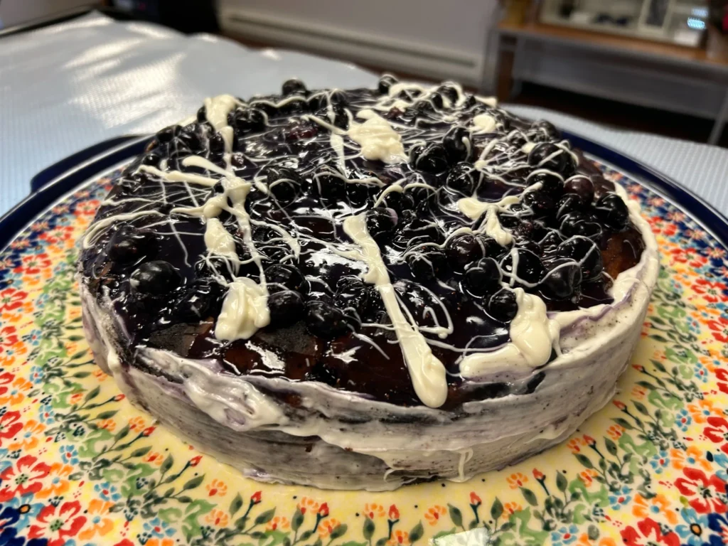 Round blueberry cake topped with berries, glaze, and white chocolate drizzle at Kat’s Café & Restaurant.