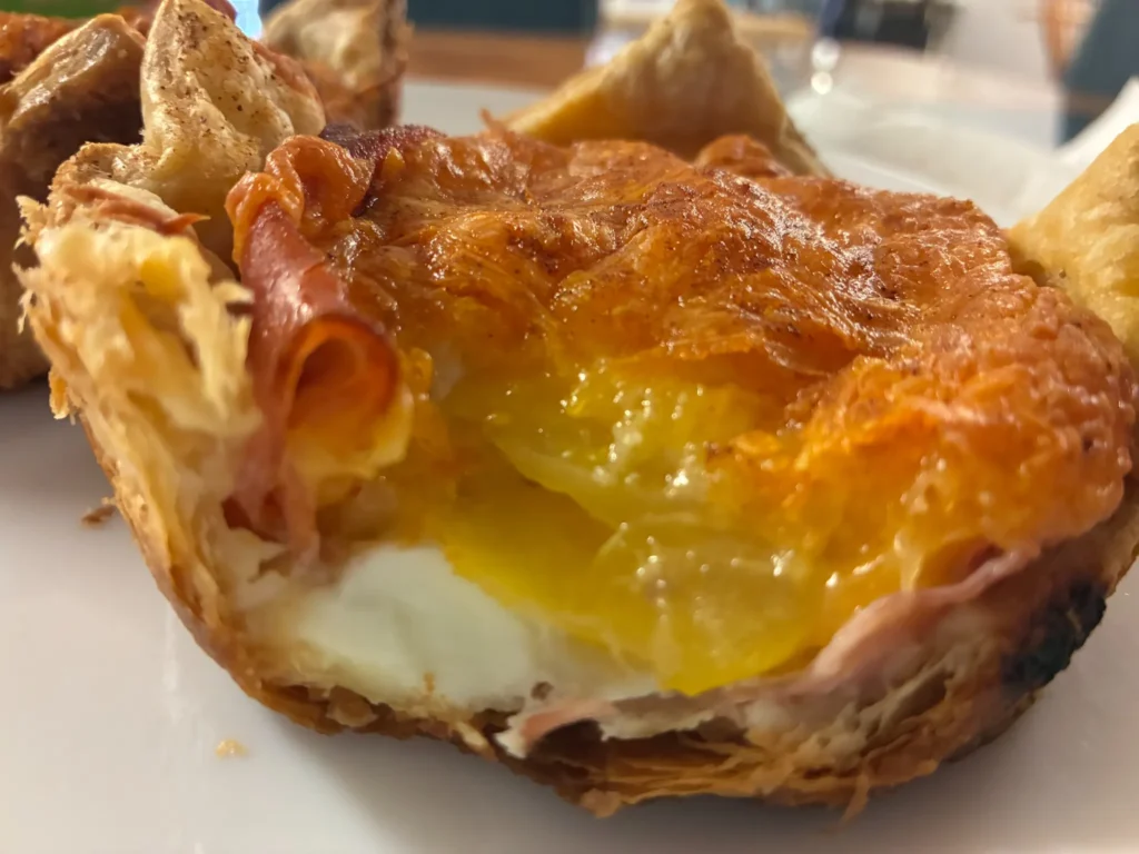 Fresh baked croissant filled with ham, fried egg, and melted cheese topping, served on a white plate at Kat’s Café & Restaurant.