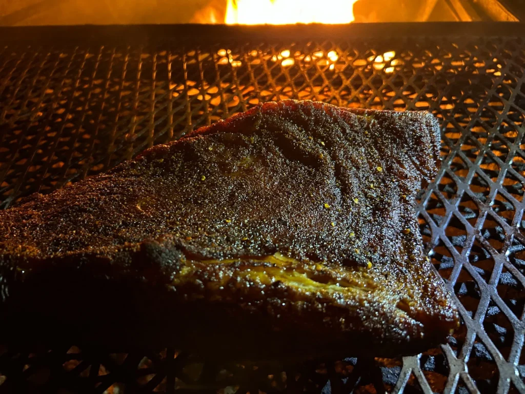 Seasoned brisket smoking on an outdoor grill over a live fire for the BBQ brisket at Kat’s Café & Restaurant.