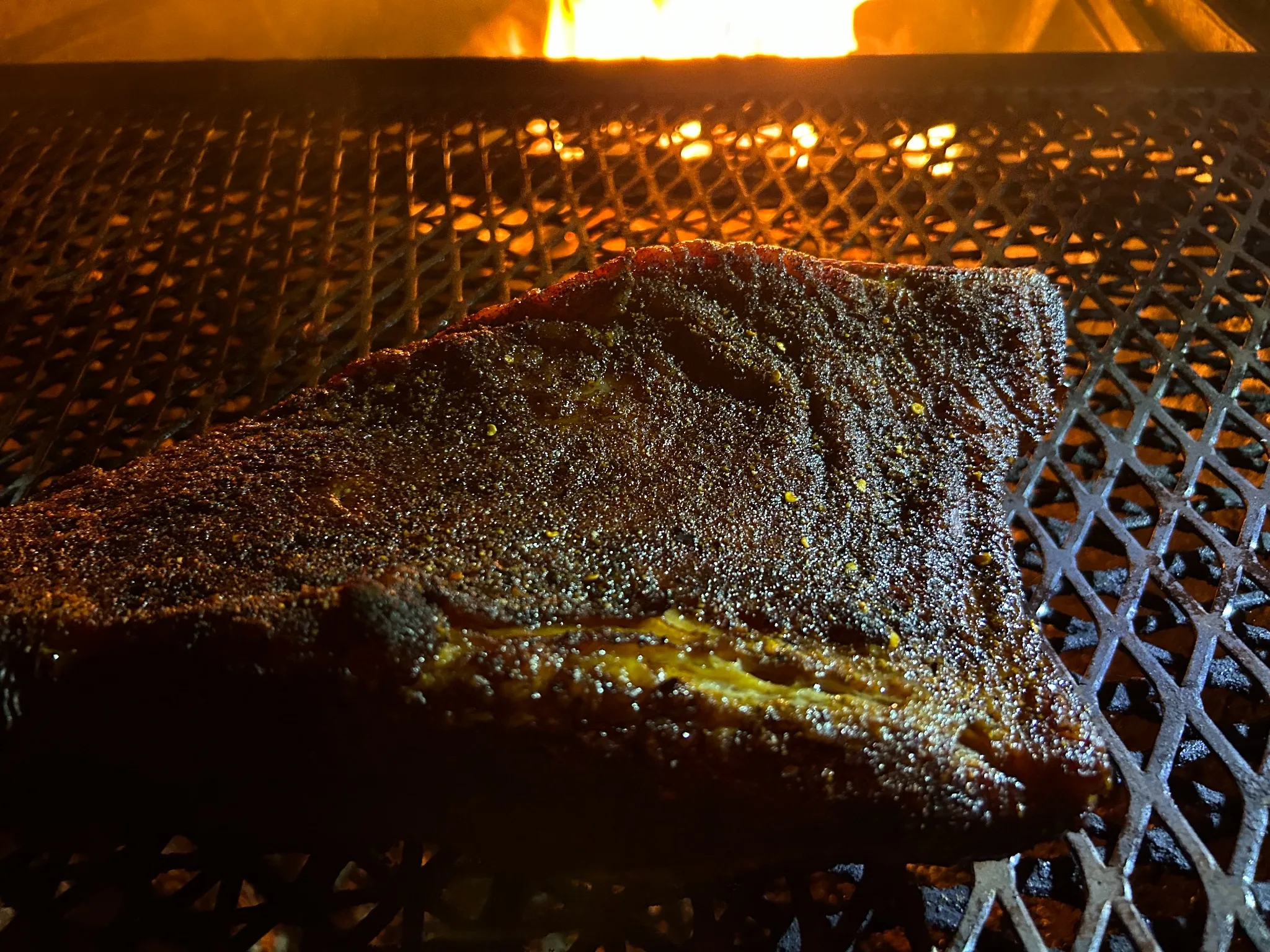 Seasoned brisket smoking on an outdoor grill over a live fire for the BBQ brisket at Kat’s Café & Restaurant.