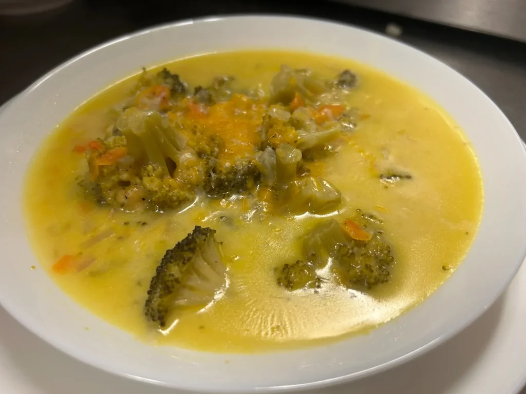 Creamy broccoli cheddar soup with broccoli florets and melted cheddar in a white bowl at Kat’s Café & Restaurant.