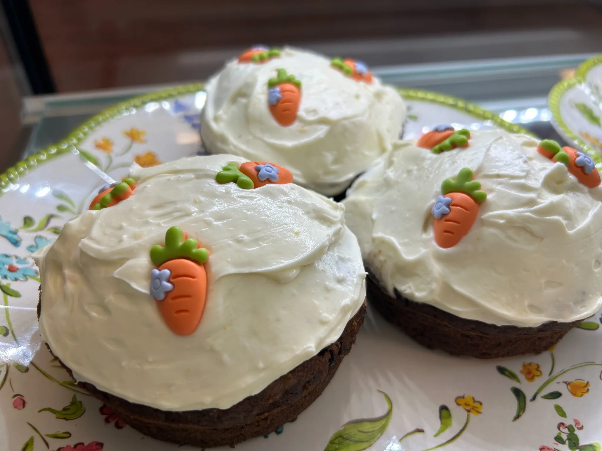 Three mini carrot cakes with cream cheese frosting and carrot decorations on a floral plate at Kat’s Café & Restaurant.