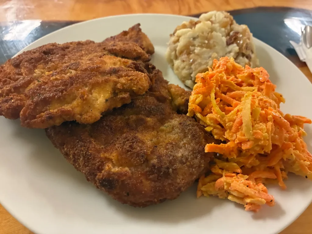 Breaded chicken cutlets served with mashed potatoes and a shredded carrot salad on a white plate at Kat’s Café & Restaurant.