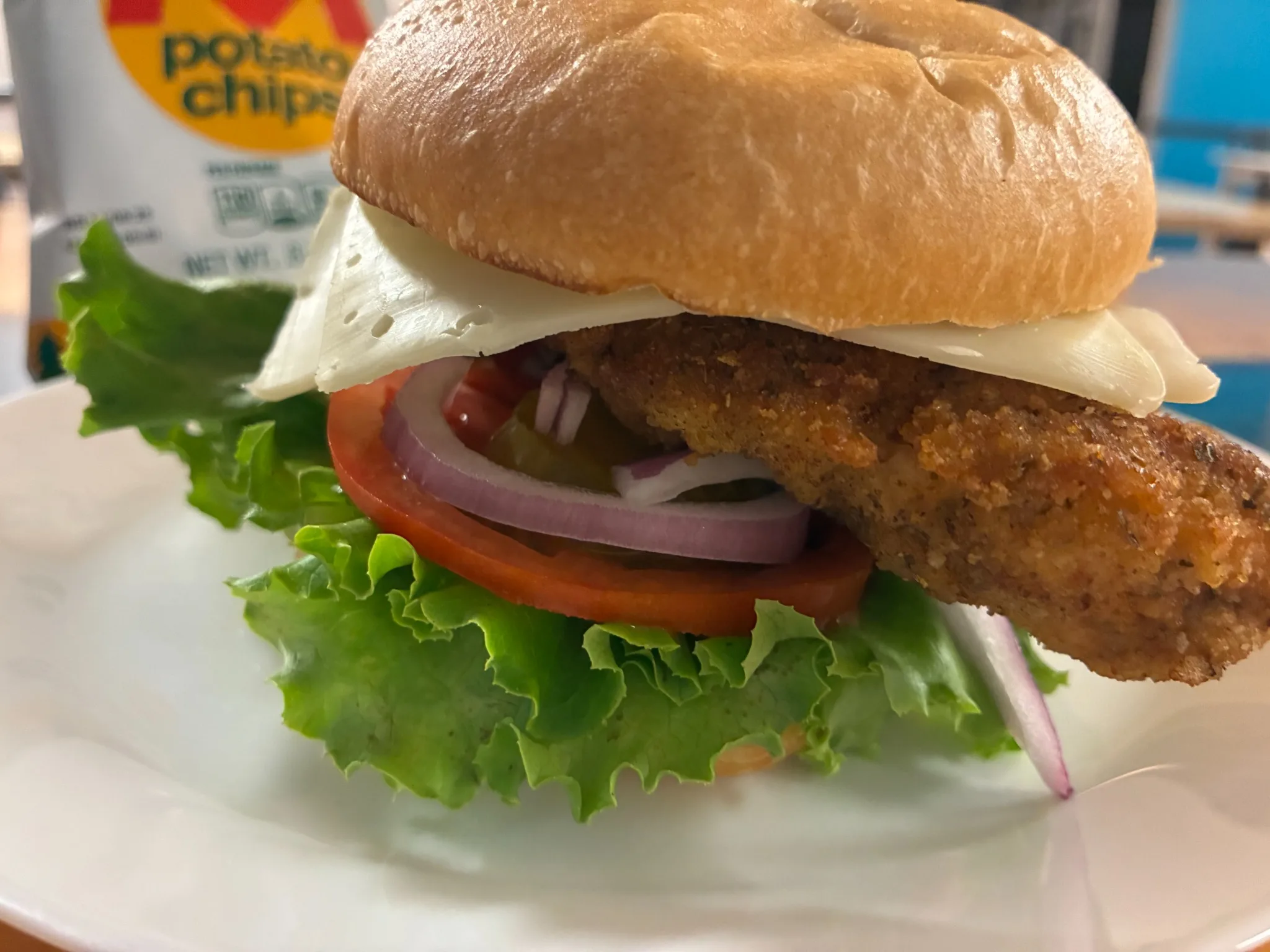 Crispy chicken cutlet sandwich with cheese, lettuce, tomato, and red onion on a fresh kaiser roll at Kat’s Café & Restaurant.